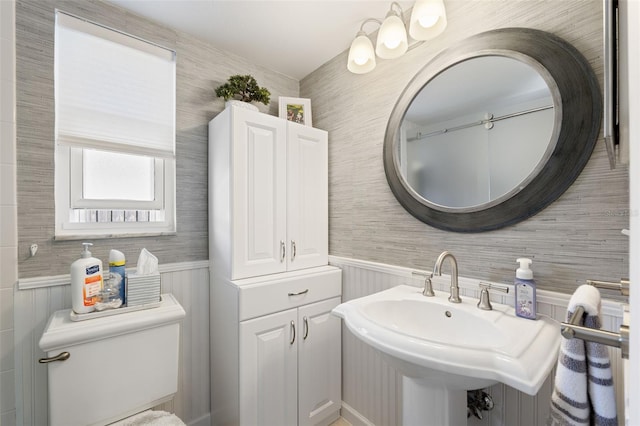 bathroom featuring wainscoting, a sink, toilet, and wallpapered walls