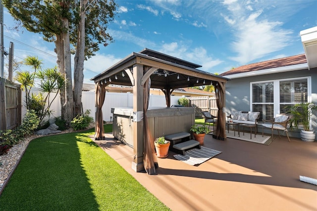 view of patio featuring a hot tub, an outdoor hangout area, a fenced backyard, and a gazebo