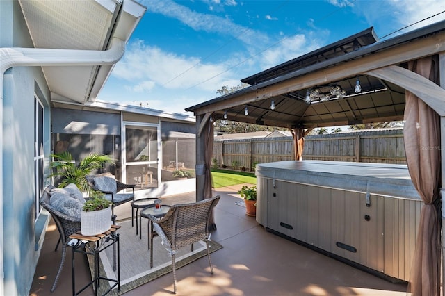 view of patio with a sunroom, a hot tub, fence, and a gazebo