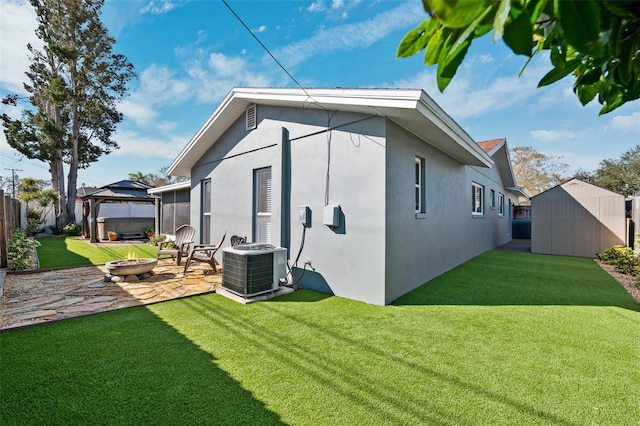 view of side of property with an outdoor fire pit, a gazebo, central air condition unit, a shed, and stucco siding