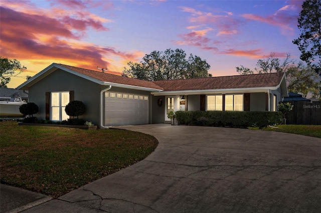 ranch-style home featuring a garage, concrete driveway, a lawn, and stucco siding