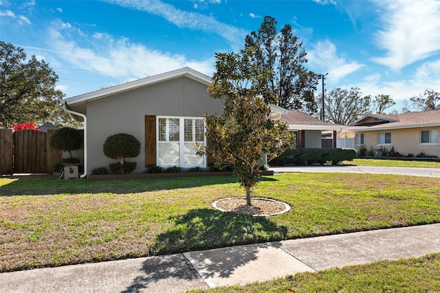 ranch-style house featuring a front yard, concrete driveway, fence, and stucco siding