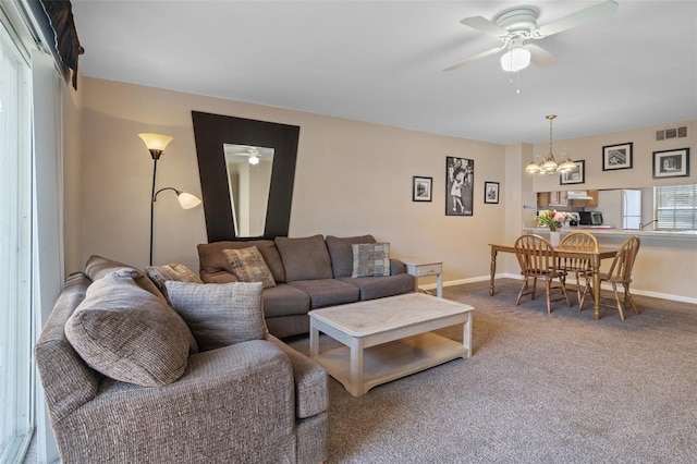 carpeted living room with ceiling fan with notable chandelier