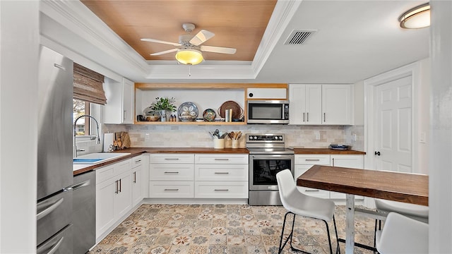 kitchen featuring appliances with stainless steel finishes, butcher block countertops, a sink, and white cabinets