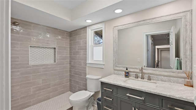 bathroom featuring toilet, a tile shower, vanity, and recessed lighting