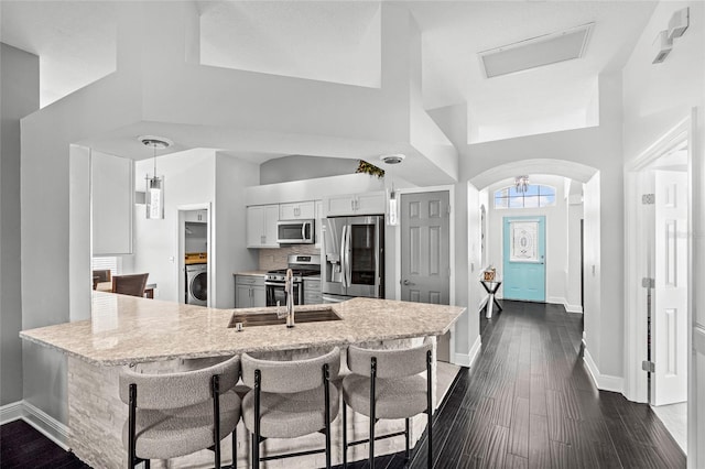 kitchen featuring white cabinetry, kitchen peninsula, stainless steel appliances, a breakfast bar, and washer / dryer