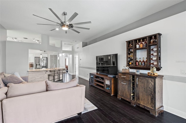 living room featuring dark wood-type flooring, ceiling fan, and indoor bar