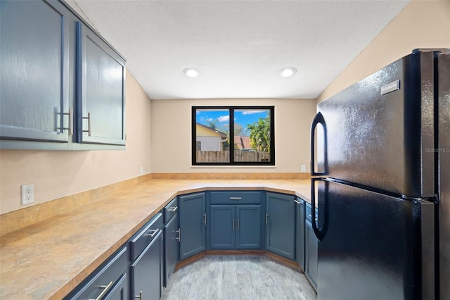 kitchen featuring blue cabinets, a textured ceiling, light countertops, and freestanding refrigerator