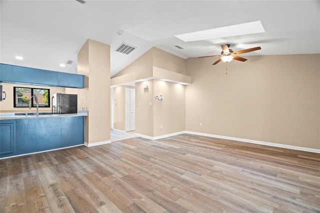 unfurnished living room with visible vents, baseboards, vaulted ceiling with skylight, wood finished floors, and a sink