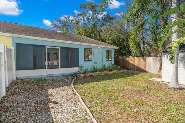 back of property with a yard, a sunroom, a shingled roof, and fence