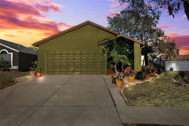 view of front facade featuring an attached garage, fence, concrete driveway, and stucco siding