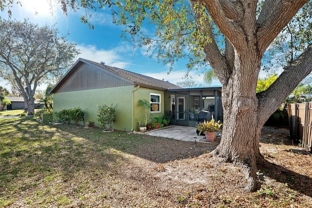 rear view of property with fence, a sunroom, a yard, stucco siding, and a patio area