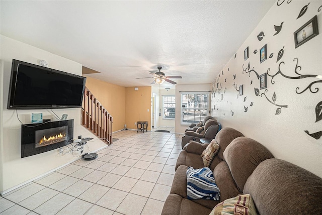 living room with light tile patterned floors, a textured ceiling, a ceiling fan, baseboards, and a glass covered fireplace