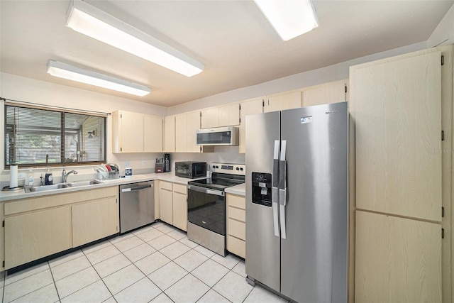 kitchen with light tile patterned floors, stainless steel appliances, cream cabinetry, light countertops, and a sink