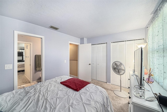 bedroom featuring a textured ceiling, carpet, two closets, and visible vents