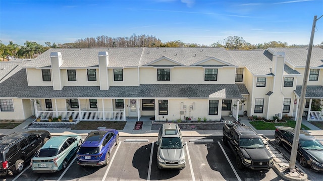 view of property with uncovered parking, roof with shingles, and a porch