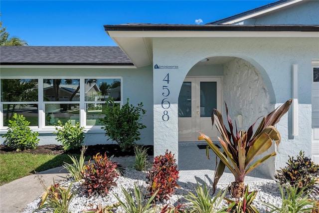 entrance to property featuring stucco siding and roof with shingles