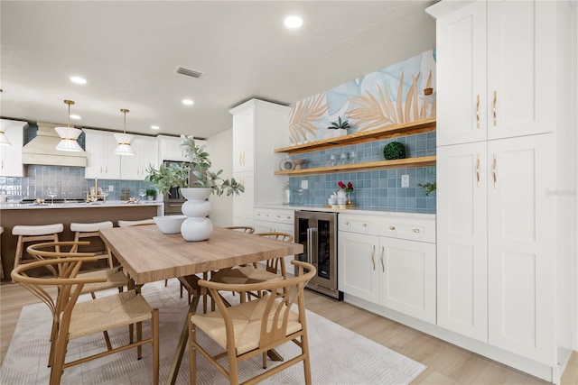 dining space with visible vents, beverage cooler, light wood-style flooring, recessed lighting, and a bar