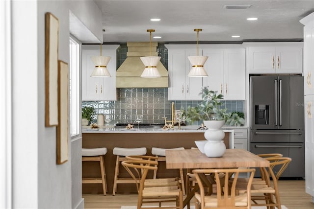 kitchen with custom exhaust hood, high end refrigerator, backsplash, and visible vents