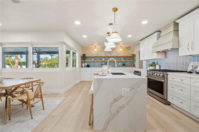 kitchen with premium range hood, a center island with sink, decorative backsplash, stainless steel stove, and a sink