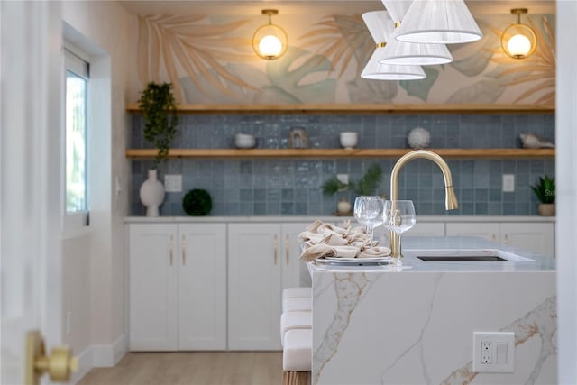 kitchen with light stone counters, open shelves, a sink, white cabinetry, and light wood-type flooring