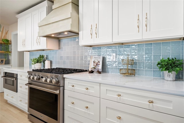 kitchen with light wood-type flooring, custom range hood, light stone counters, white cabinetry, and stainless steel appliances