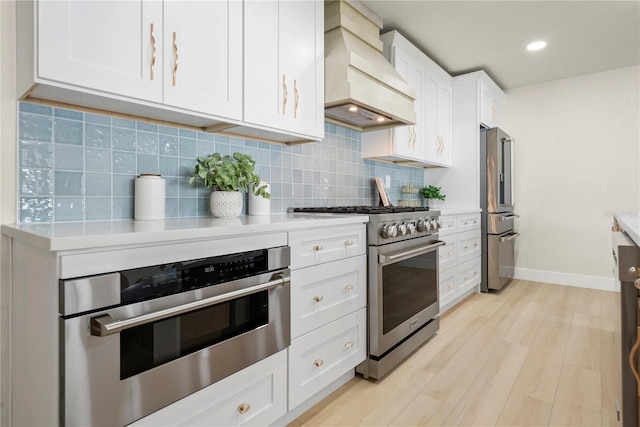 kitchen featuring high quality appliances, backsplash, light wood finished floors, custom exhaust hood, and light countertops