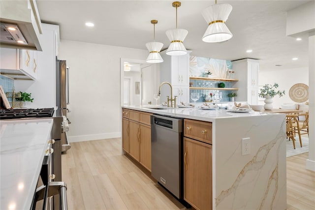 kitchen featuring a kitchen island with sink, a sink, light wood-style floors, appliances with stainless steel finishes, and wall chimney exhaust hood