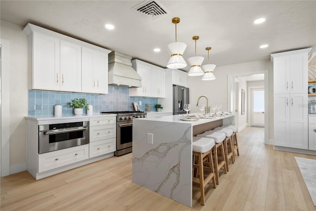 kitchen featuring visible vents, light wood-style flooring, tasteful backsplash, stainless steel appliances, and custom exhaust hood