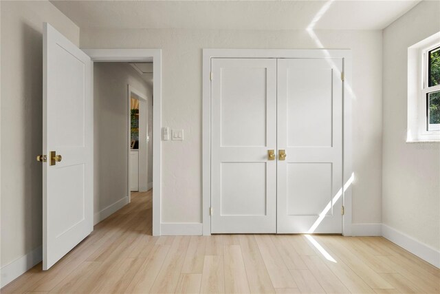 unfurnished bedroom featuring light wood finished floors, a closet, and baseboards