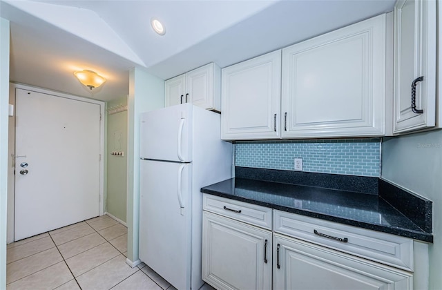 kitchen with light tile patterned floors, tasteful backsplash, freestanding refrigerator, white cabinets, and vaulted ceiling