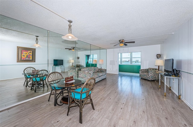 dining area with light wood-type flooring, a ceiling fan, and a textured ceiling