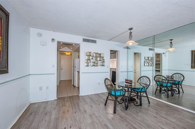 unfurnished dining area featuring light wood finished floors, baseboards, visible vents, and a textured ceiling