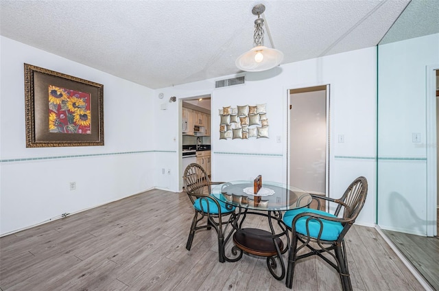 dining room featuring light wood-style floors, visible vents, and a textured ceiling