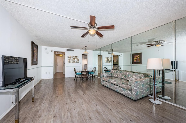 living area featuring ceiling fan, a textured ceiling, wood finished floors, and visible vents