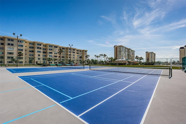 view of tennis court with a view of city and fence