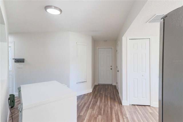 hall featuring light wood-style floors, visible vents, and baseboards