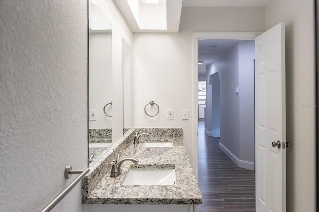 bathroom featuring double vanity, baseboards, a sink, and wood finished floors