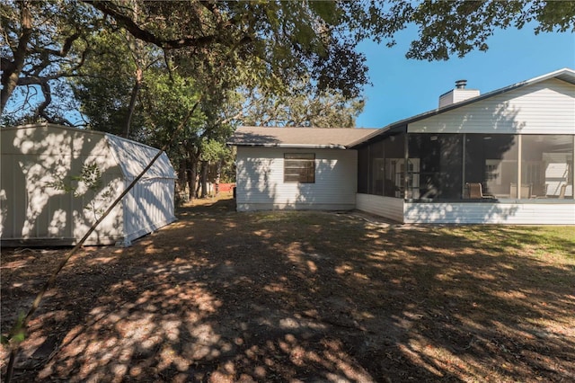 rear view of property featuring an outbuilding, a sunroom, a lawn, a shed, and a chimney