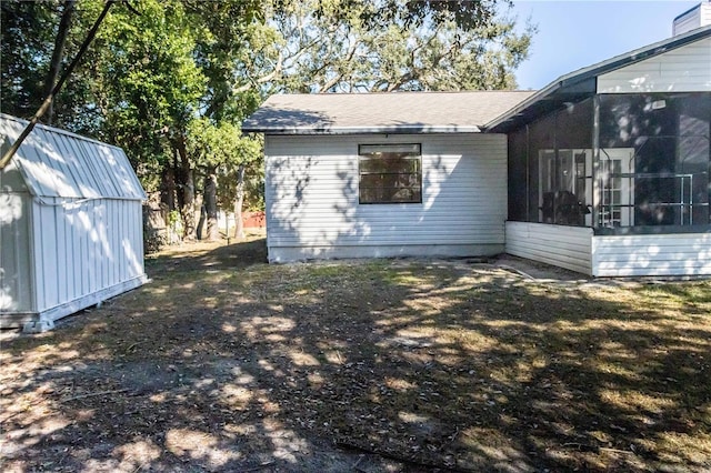 view of property exterior with a storage shed, a sunroom, and an outbuilding