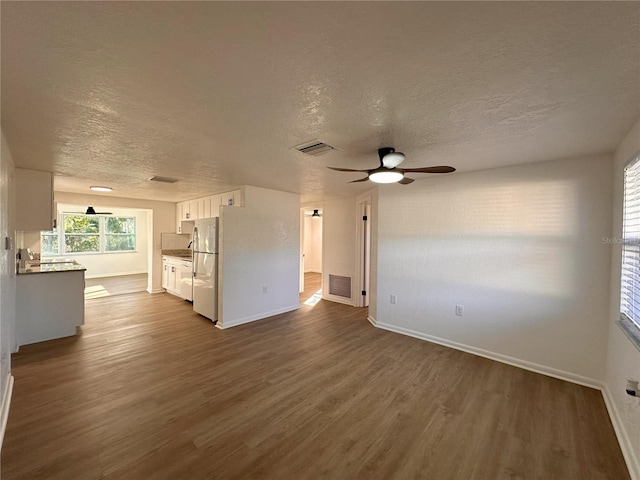 unfurnished living room with a textured ceiling, dark wood-type flooring, and visible vents