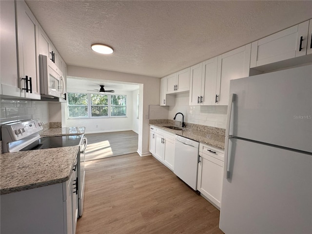 kitchen featuring tasteful backsplash, light wood-style floors, white cabinetry, a sink, and white appliances