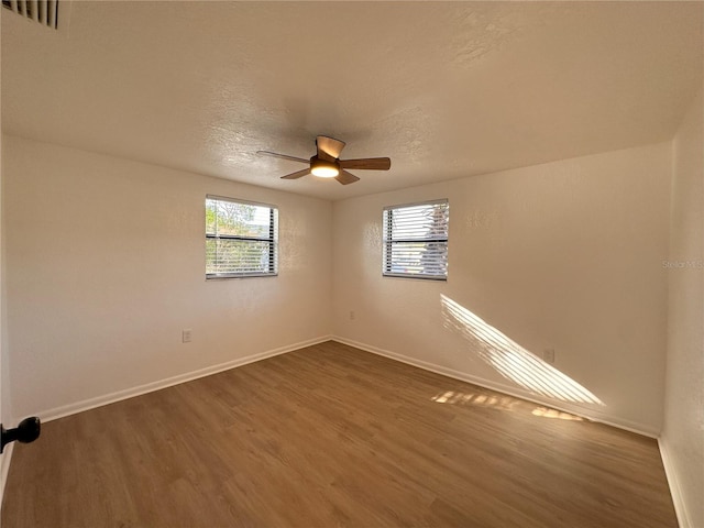 spare room with ceiling fan, plenty of natural light, wood finished floors, and baseboards