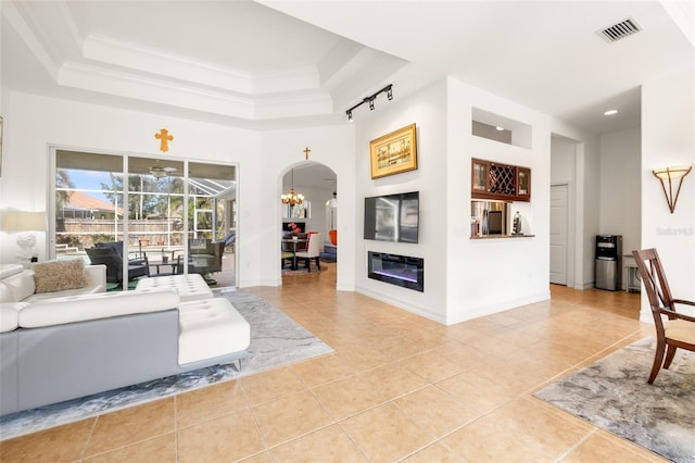 tiled living room with a tray ceiling, a towering ceiling, crown molding, and a notable chandelier