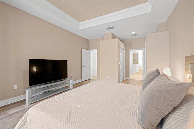 bedroom featuring a raised ceiling, light hardwood / wood-style floors, ensuite bathroom, and ornamental molding