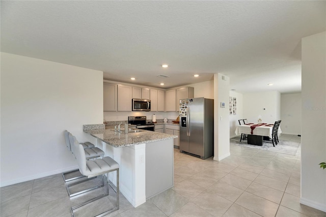 kitchen featuring appliances with stainless steel finishes, light stone counters, a kitchen breakfast bar, a peninsula, and gray cabinets