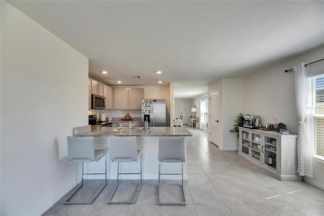 kitchen featuring light tile patterned floors, a breakfast bar area, stone countertops, stainless steel appliances, and a peninsula