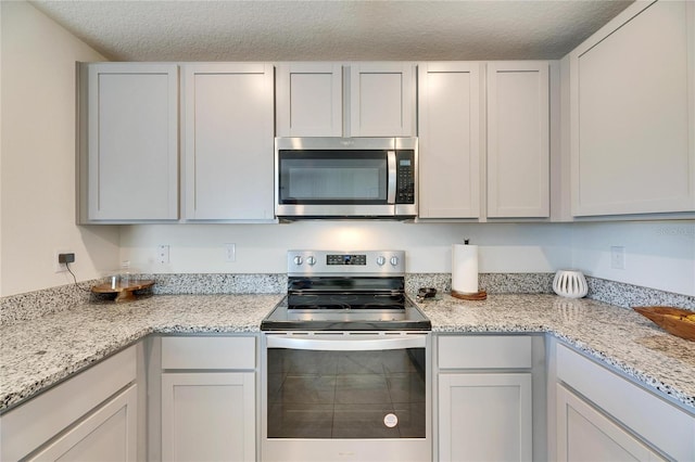 kitchen with a textured ceiling, stainless steel appliances, and light stone countertops