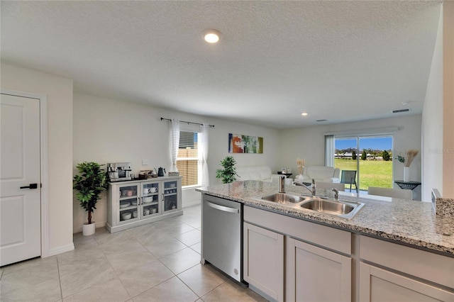 kitchen featuring light stone counters, stainless steel dishwasher, light tile patterned flooring, a sink, and a textured ceiling