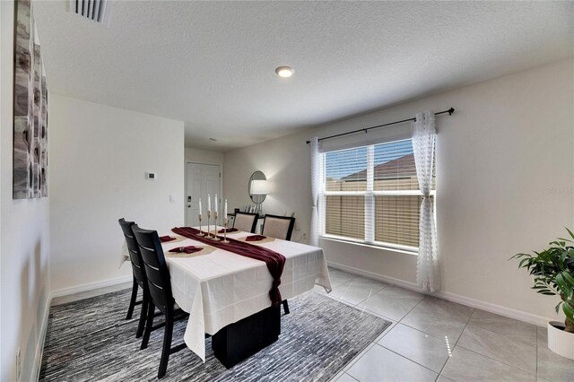 dining space with light tile patterned floors, baseboards, visible vents, and a textured ceiling